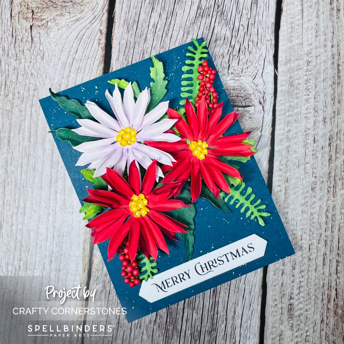 Handmade Christmas card featuring layered red and pink paper flowers, green foliage, and “Merry Christmas” sentiment created with Spellbinders Serenity Garden Collection Poetic Foliage Set