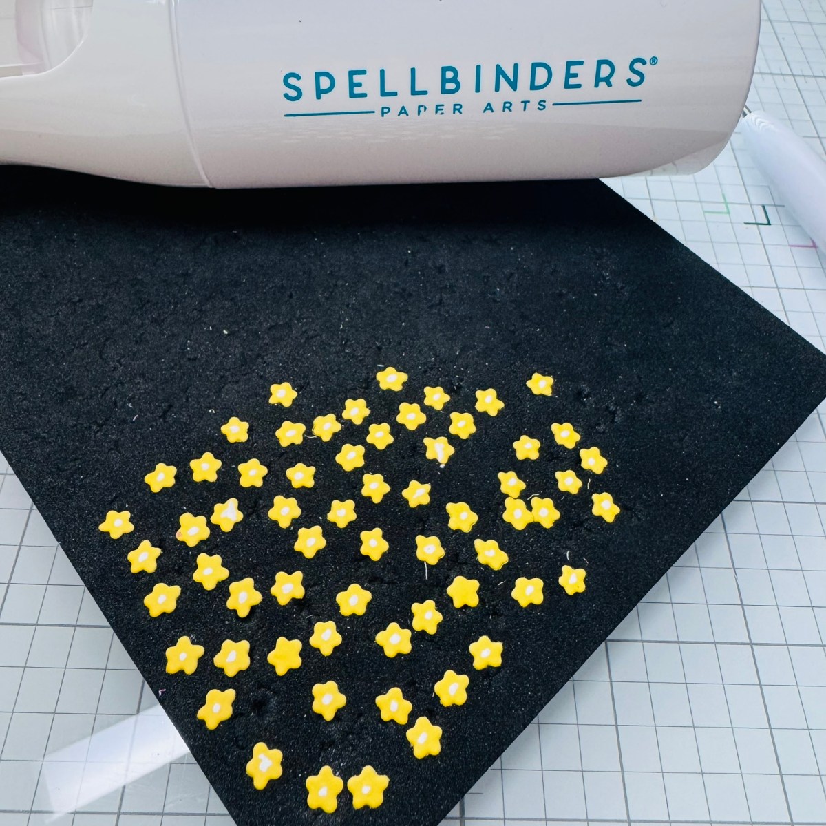 Crafting setup showing Spellbinders Paper Arts tool and yellow flower centers being shaped on a foam mat for handmade card embellishments.