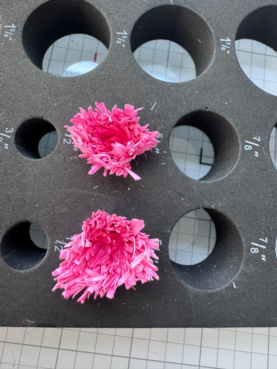 Two pink paper flowers placed on a foam shaping mat with circular measurement guides for crafting
