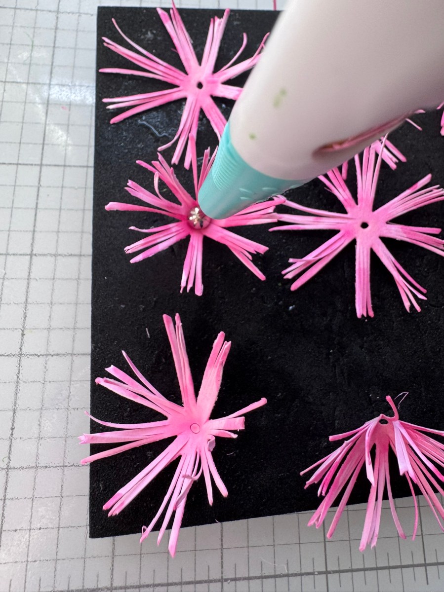 Pink paper flowers being assembled on a foam mat using a crafting stylus